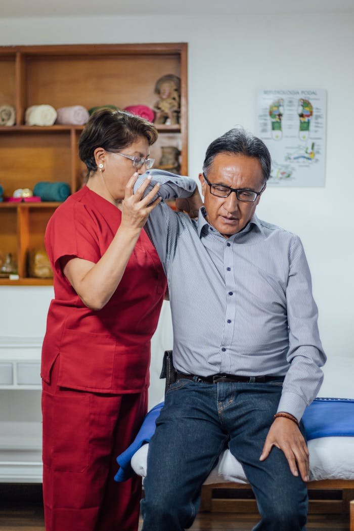 A therapist guides a senior adult in shoulder rehabilitation therapy indoors.