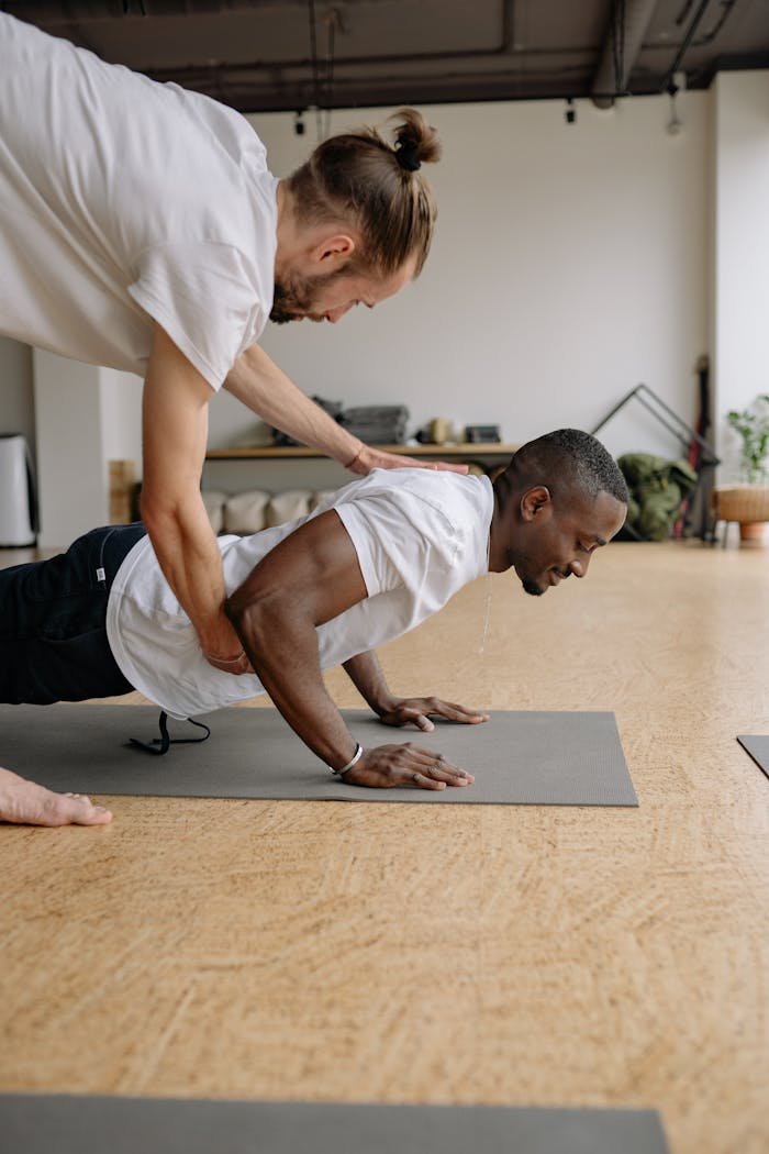 A personal trainer helps a client perform push-ups indoors on gym mats.